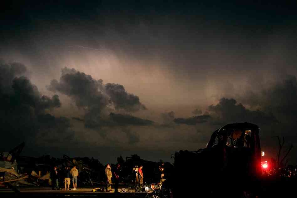 Emergency workers wait for a medical team after finding a body in a tornado-ravaged car. A twister tore through nearly six miles of the city Sunday. 
