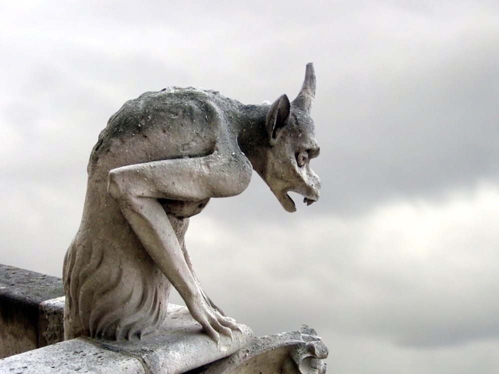A creepy gargoyle looks onto an overcast sky.