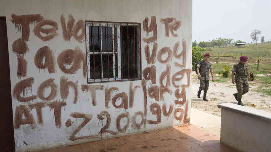 Soldiers walk past part of a message written in blood at the site of a massacre at a ranch in northern Guatemala on May 16. The message is a warning to Otto Salguero — the owner of the ranch, according to local media. Guatemalan authorities blame the killings on the Mexican drug cartel Los Zetas. Soldiers walk past part of a message written in blood at the site of a massacre at a ranch in northern Guatemala on May 16. The message is a warning to Otto Salguero — the owner of the ranch, according to local media. Guatemalan authorities blame the killings on the Mexican drug cartel Los Zetas.