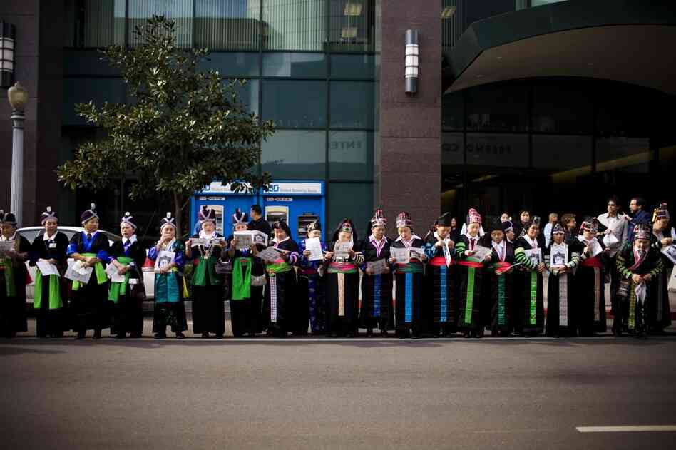 Hmong women wearing traditional clothing line the streets during the funeral procession.