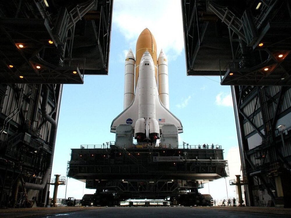 Framed in the doors of the Kennedy Center's Vehicle Assembly Building, the crawler begins the long journey toward Launch Pad 37B with space shuttle Discovery in April 2005.  This enormous cross between a tank and a cargo ship is the largest self-powered land vehicle in the world.
