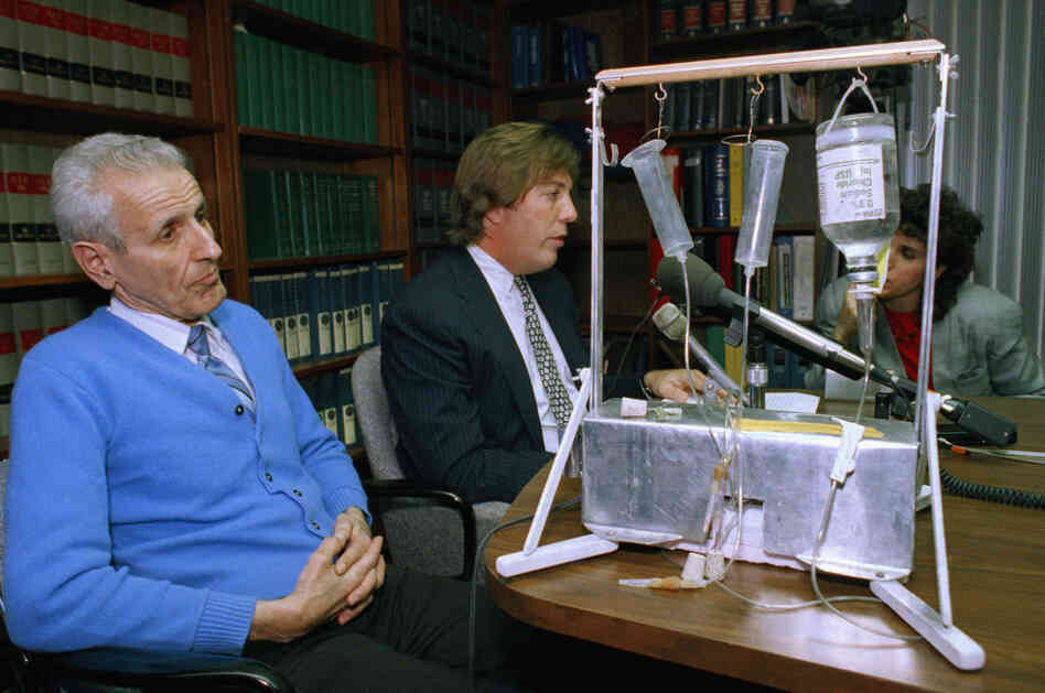 Kevorkian (left), then 62, listens as his attorney talks with reporters, Feb. 6, 1991. Pictured on the table is the machine he used to inject lethal drugs into 130 people. 