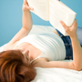 A girl lies on her back reading a book.