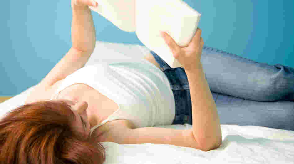 A girl lies on her back reading a book.