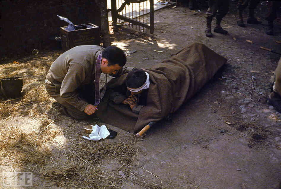 An American Army chaplain kneels next to a wounded soldier in order to administer the Eucharist and last rites.