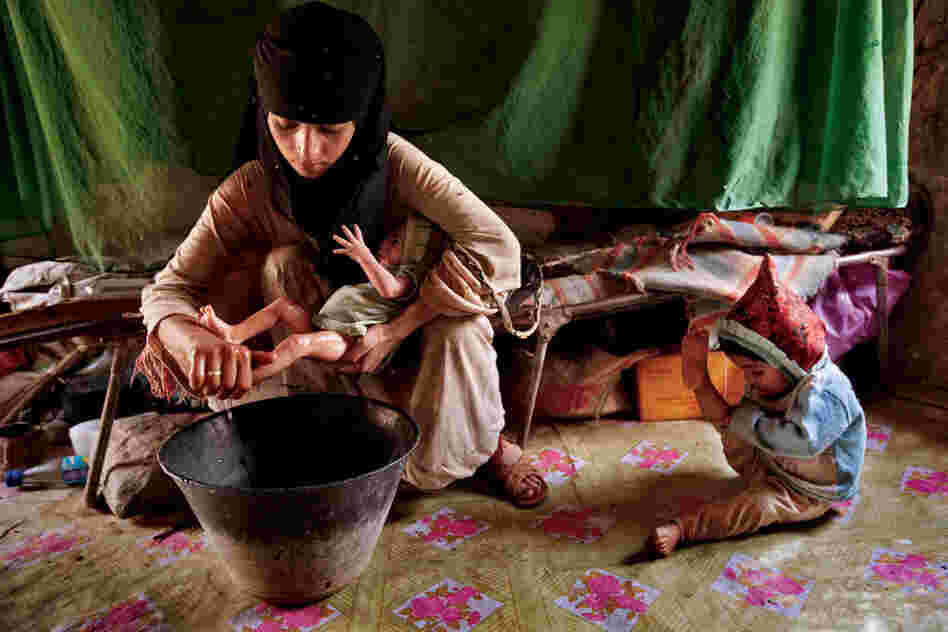Asia, a 14-year-old mother, washes her new baby girl at home in Hajjah while her 2-year-old daughter plays. Asia is still bleeding and ill from childbirth yet has no education or access to information on how to care for herself.