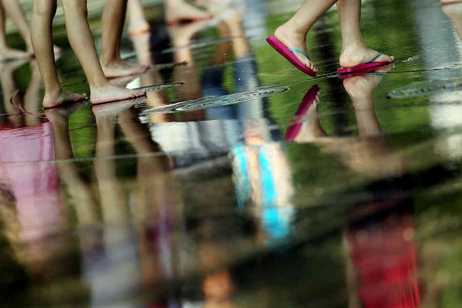 Children's feet are reflected in a fountain at Battery Park in New York City. Some schools in the Northeast planned to close early Thursday so students would not have to suffer in buildings without air conditioning. 