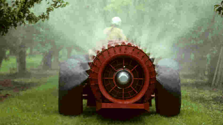 A pesticide sprayer rolls through an apple orchard.