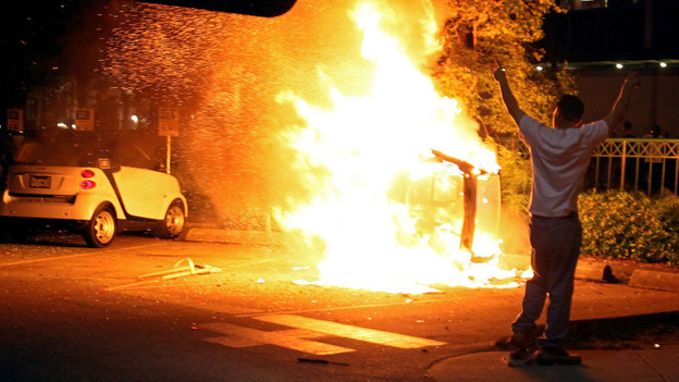 A person walks in front of a burning vehicle after riots break out following the Vancouver Canucks' loss in the NHL finals.