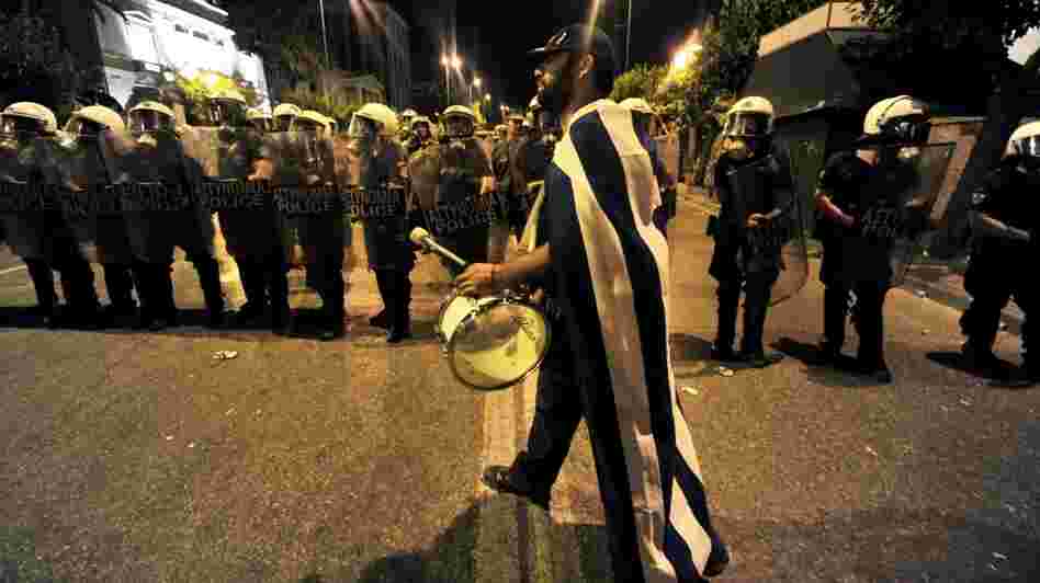 A demonstrator plays drum in front of riot police outside the Greek Parliament in Athens. The protesters aren't the usual leftists and trade unionists with red banners. They're mostly middle-class Greeks waving the white and blue national flag.