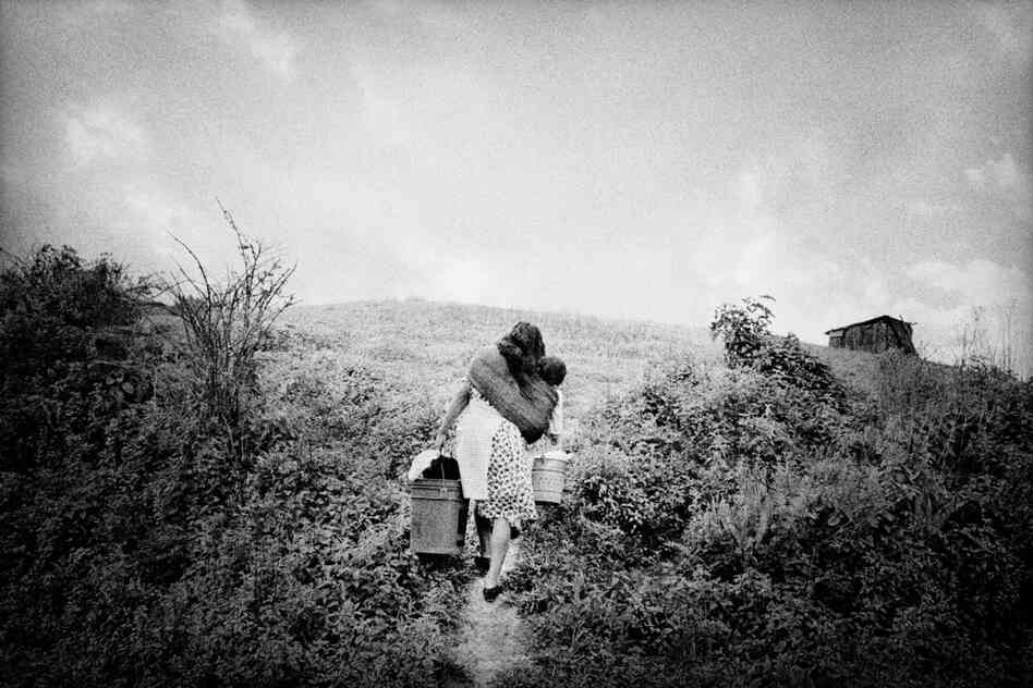 A woman returns home laden with her infant and household supplies.