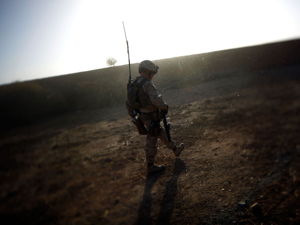 A Marine walks along a  mud wall while conducting a search and clearing operation in Afghanistan's Helmand province, as the dust from a wheat thrashing machine falls like snow.