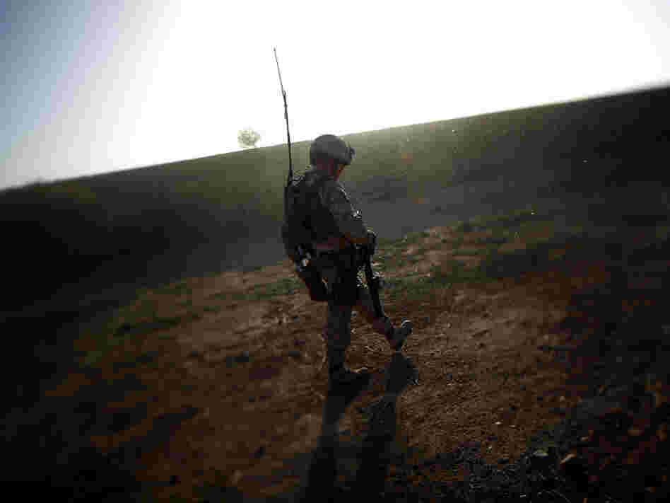 A Marine walks along a  mud wall while conducting a search and clearing operation in Afghanistan's Helmand province, as the dust from a wheat thrashing machine falls like snow.