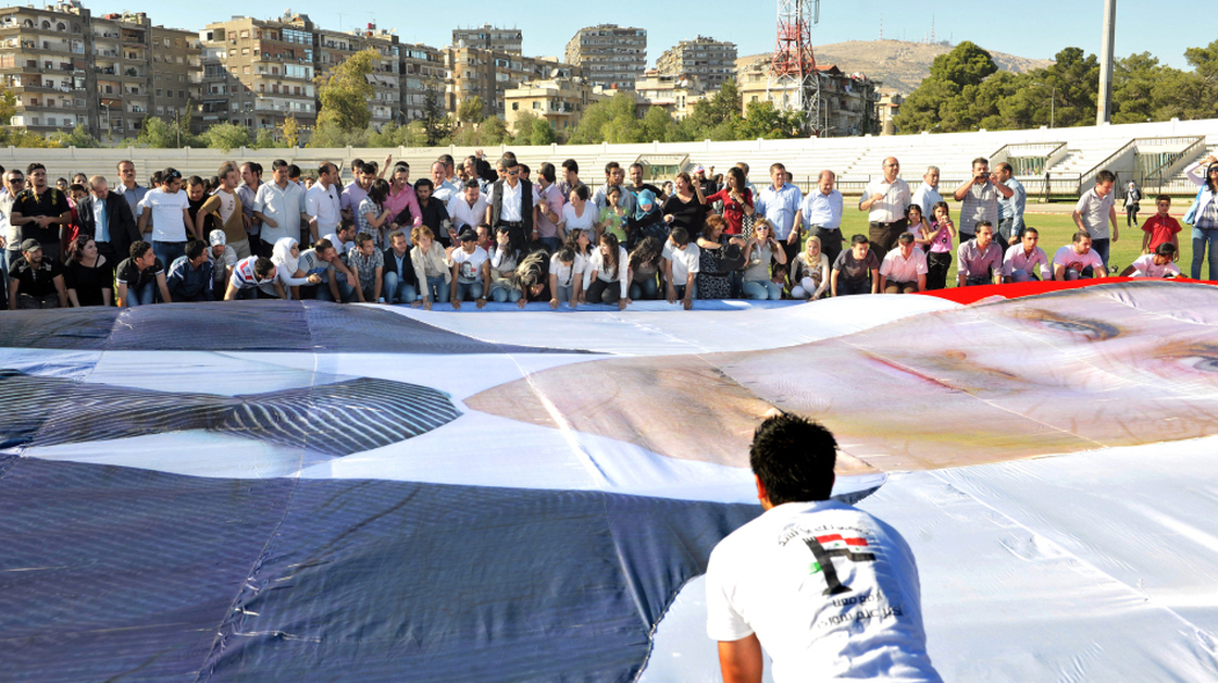 Regime supporters prepare to mount a huge poster of Syrian President Bashar al-Assad at Al-Jalaa Stadium in Damascus.