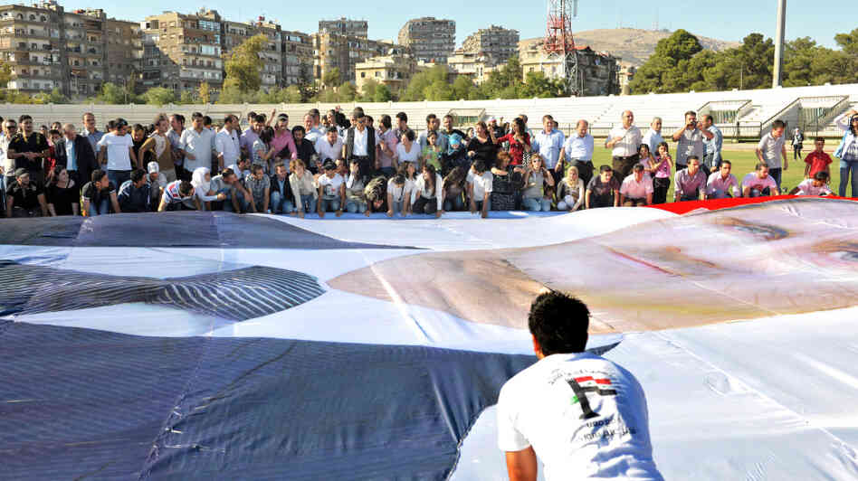 Regime supporters prepare to mount a huge poster of Syrian President Bashar al-Assad at Al-Jalaa Stadium in Damascus.