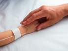 A man holds the hand of a child with an intravenous line in place. A man holds the hand of a child with an intravenous line in place.