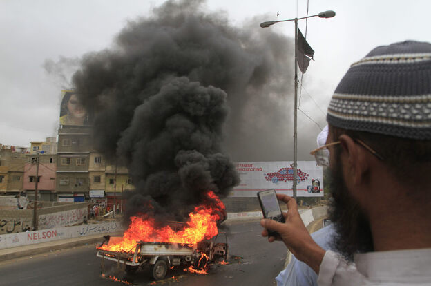 A man takes pictures of a vehicle burned by angry protesters in Karachi, Pakistan.