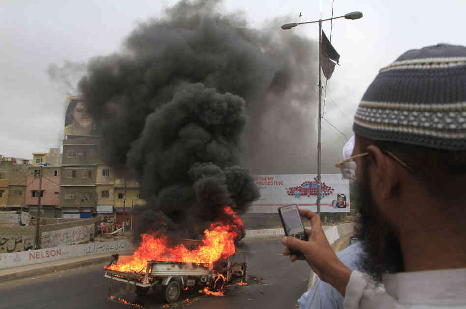 A man takes pictures of a vehicle burned by angry protesters in Karachi, Pakistan.