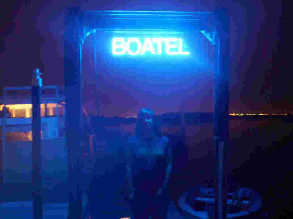 Constance Hockaday, the creator of the Boatel, stands under the sign announcing her art project/hotel at Marina 59 on Jamaica Bay in Queens, New York.