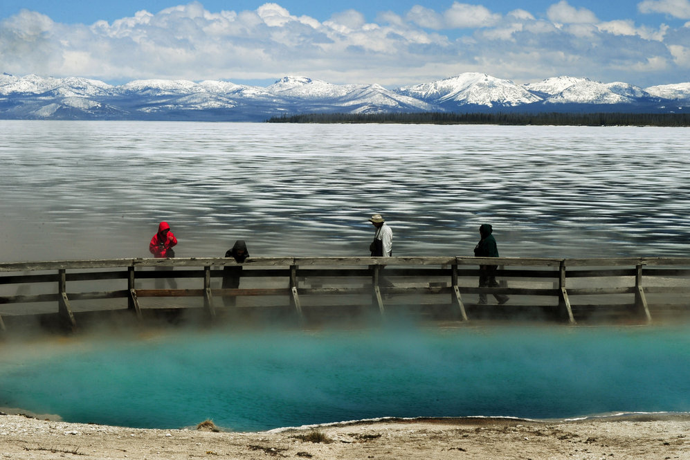 Tourists walk beside a hot spring and the partially frozen Yellowstone Lake at the West Thumb Geyser Basin.