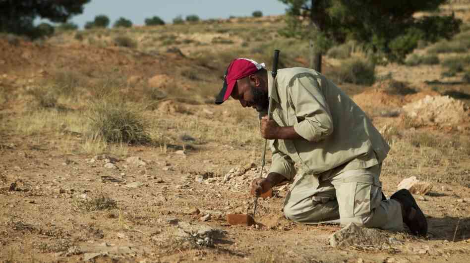 Milad Saadi clears the dirt around a brick of plastic explosives that he discovered lying on top of a T-AB-1 anti-personnel mine. Milad Saadi clears the dirt around a brick of plastic explosives that he discovered lying on top of a T-AB-1 anti-personnel mine.