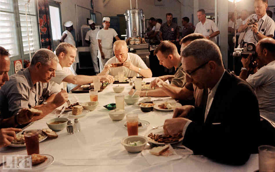 Glenn eats a meal, surrounded by media, prior to his historic February 1962 orbital flight. 