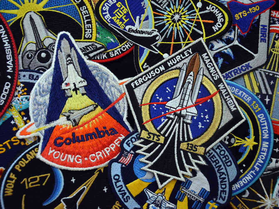 Every space shuttle mission had its own mission emblem, designed and worn by the crews. Centered in this photo are the embroidered patches for the first and last missions, STS-1 and STS-135. The STS-1 emblem is a rare version, produced only for the astronauts and NASA employees. The souvenir edition was slightly different.