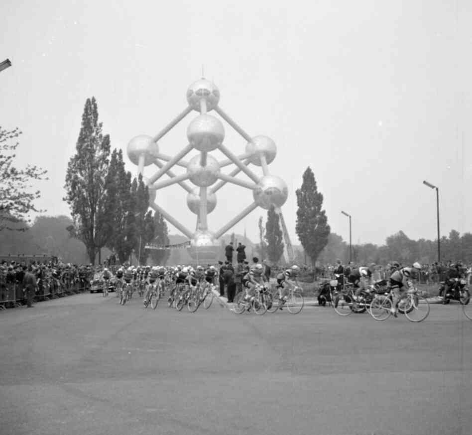 Racing cyclists pass the Atomium, a monument in Brussels, 1960.