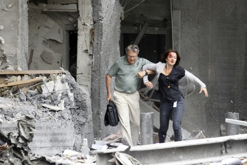 A man helps a wounded woman evacuate a building. 