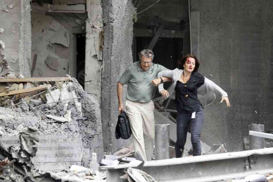 A man helps a wounded woman evacuate a building. 