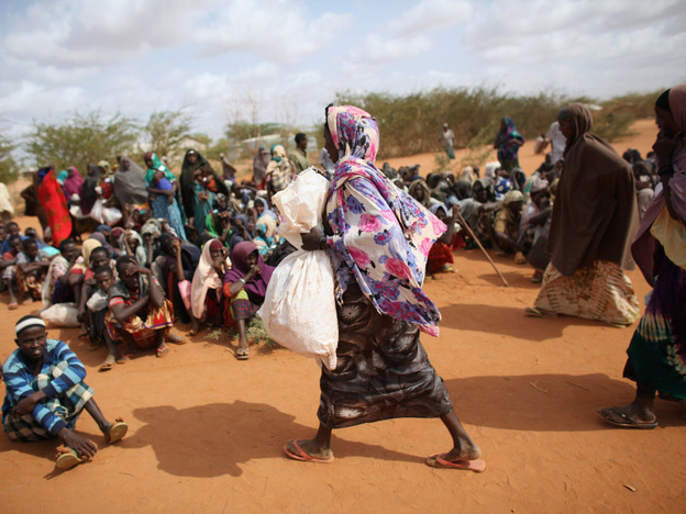 A Somali refugee woman carries a bag of food aid at the entrance to the registration area of the Dadaab refugee settlement in Kenya. While refugees receive international humanitarian aid, local Kenyans fighting drought get sacks of rice, beans and oil from the government.