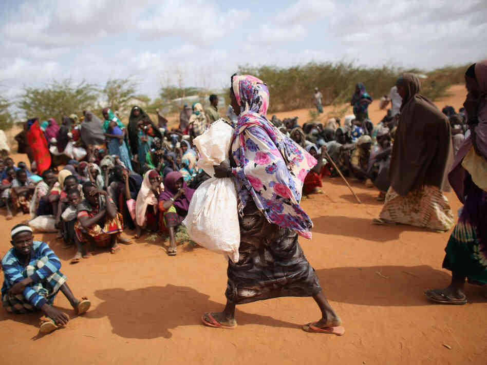 A Somali refugee woman carries a bag of food aid at the entrance to the registration area of the Dadaab refugee settlement in Kenya. While refugees receive international humanitarian aid, local Kenyans fighting drought get sacks of rice, beans and oil from the government.
