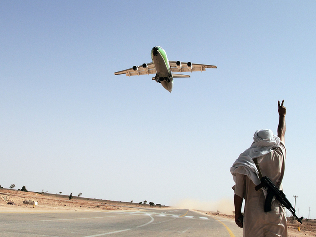 A Libyan rebel fighter flashes a victory sign as an aircraft carrying supplies for the rebels departs along a guarded mile-long stretch of road being used as runway, outside of Rhybat in western Libya, on July 19.