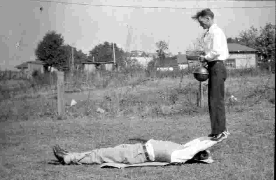 A man holds another man holding a weight.