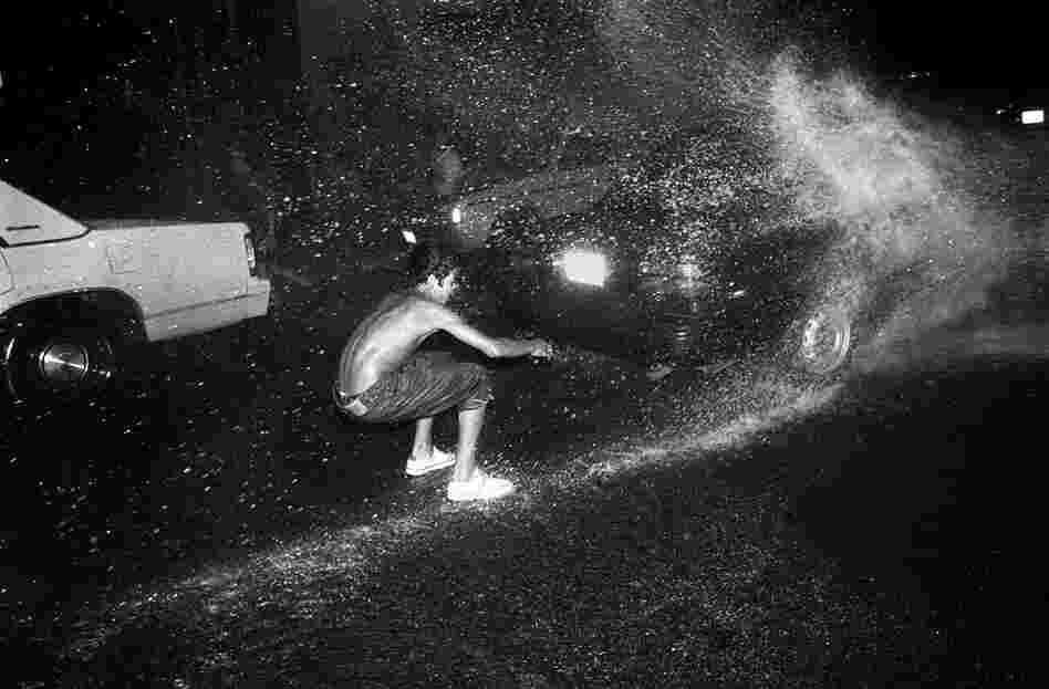 A teenage boy water "skis" on water from a fire hydrant, 1990s.