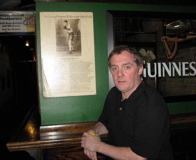 Michael Harvey stands next to a poster of his great-great-uncle Charlie Kelly at his Lincoln Park bar. Harvey's main character, Michael Kelly, was named after Charlie's father.
