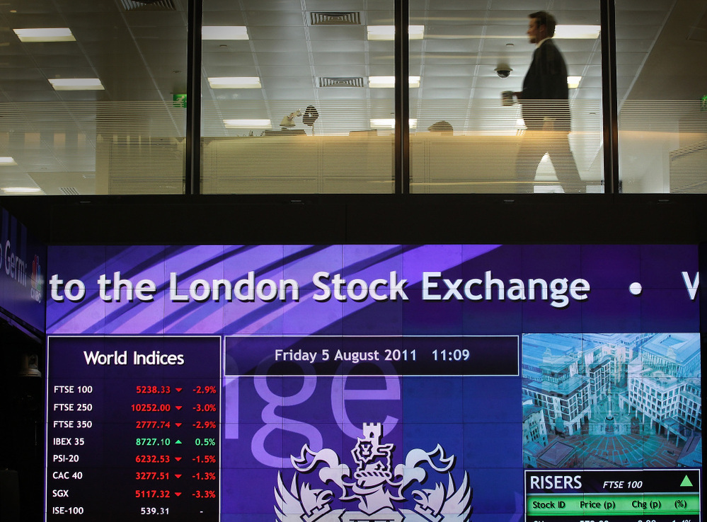 A worker walks past screens showing stock market price falling at The London Stock Exchange on August 5.