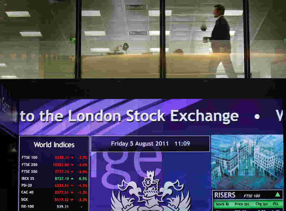 A worker walks past screens showing stock market price falling at The London Stock Exchange on August 5.