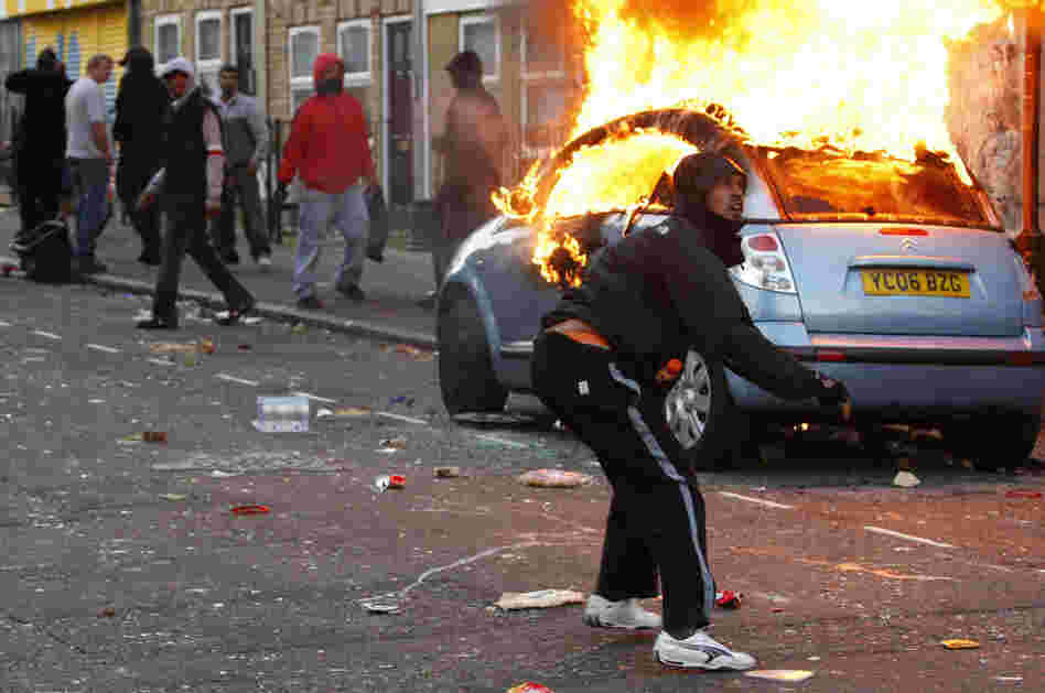 A rioter throws a rock at riot police in Clarence Road in Hackney, London, Monday. Rioting and looting continued into the night Monday in parts of London, as well as in Birmingham. The unrest was prompted by the initial rioting in Tottenham and then in Brixton on Sunday night.