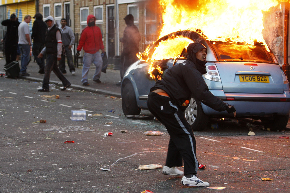 A rioter throws a rock at riot police in Clarence Road in Hackney, London, Monday. Rioting and looting continued into the night Monday in parts of London, as well as in Birmingham. The unrest was prompted by the initial rioting in Tottenham and then in Brixton on Sunday night.