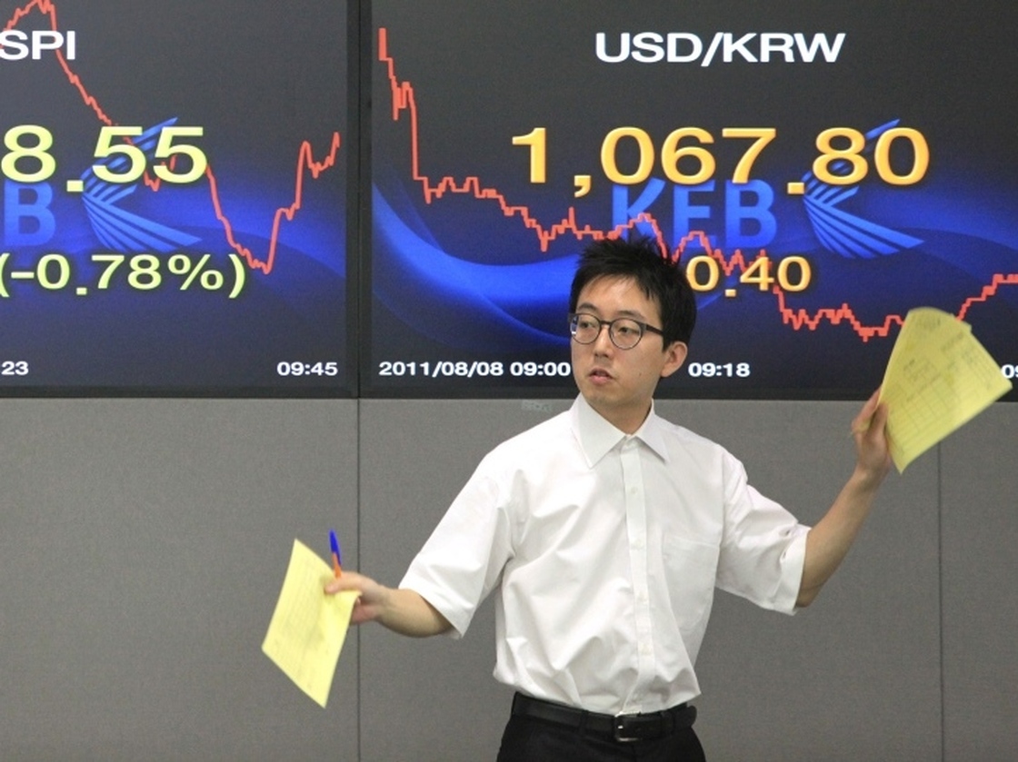 A currency trader gestures Monday in front of screens showing the Korea Composite Stock Price Index, left, and the exchange rate between the U.S. dollar and the South Korean won at the Korea Exchange Bank headquarters in Seoul, South Korea.