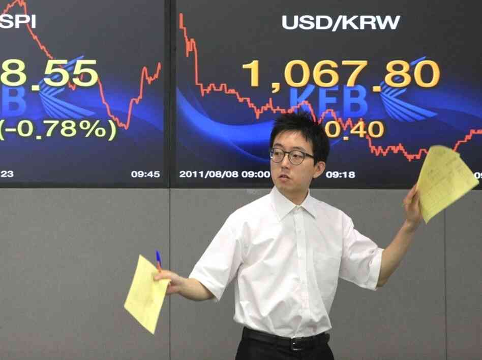 A currency trader gestures Monday in front of screens showing the Korea Composite Stock Price Index, left, and the exchange rate between the U.S. dollar and the South Korean won at the Korea Exchange Bank headquarters in Seoul, South Korea.