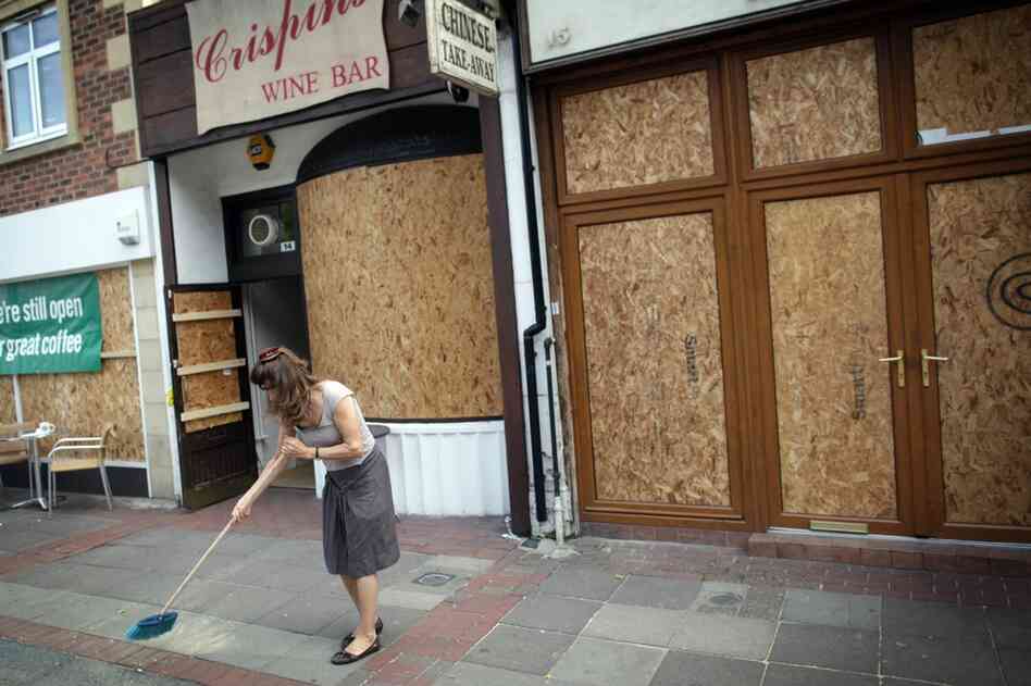 A shop owner sweeps up outside her property in Ealing, London on Aug. 10. After three nights of rioting and looting in and around London, the chaos has spread to other cities around Britain.  