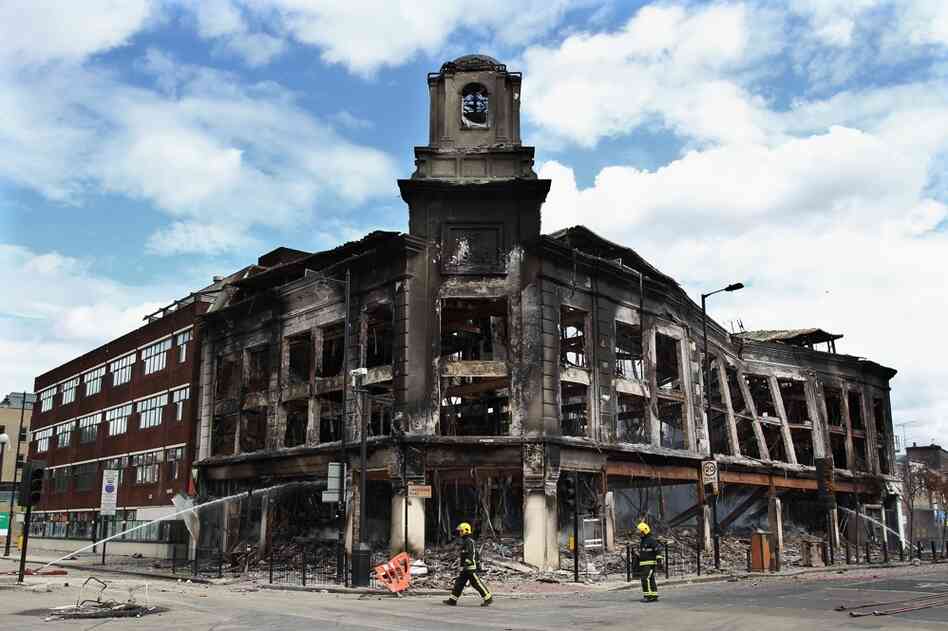 Fireman walk past the smoldering remains of a burned-out building after riots on Tottenham High Road in North London, Aug. 7. 