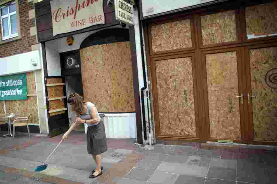 A shop owner sweeps up outside her property in Ealing, London on Aug. 10. After three nights of rioting and looting in and around London, the chaos has spread to other cities around Britain.  