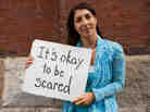 One of women in the video holds up a sign that says, "It's okay to be scared."