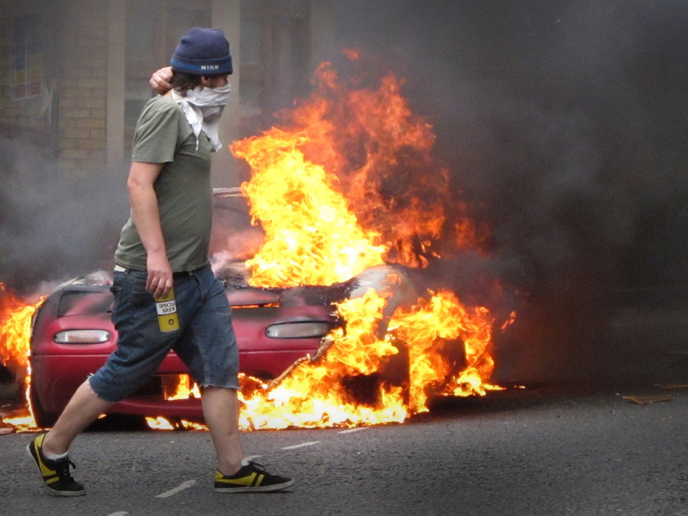 This masked man walked past a burning car in London on Monday (Aug. 8, 2011).