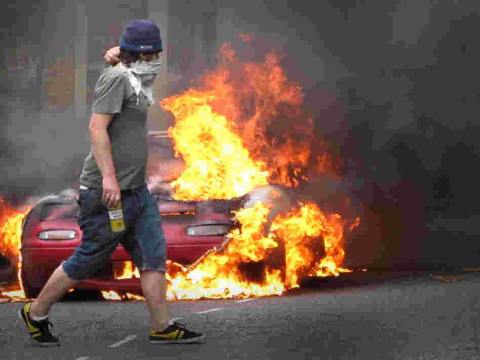 This masked man walked past a burning car in London on Monday (Aug. 8, 2011).