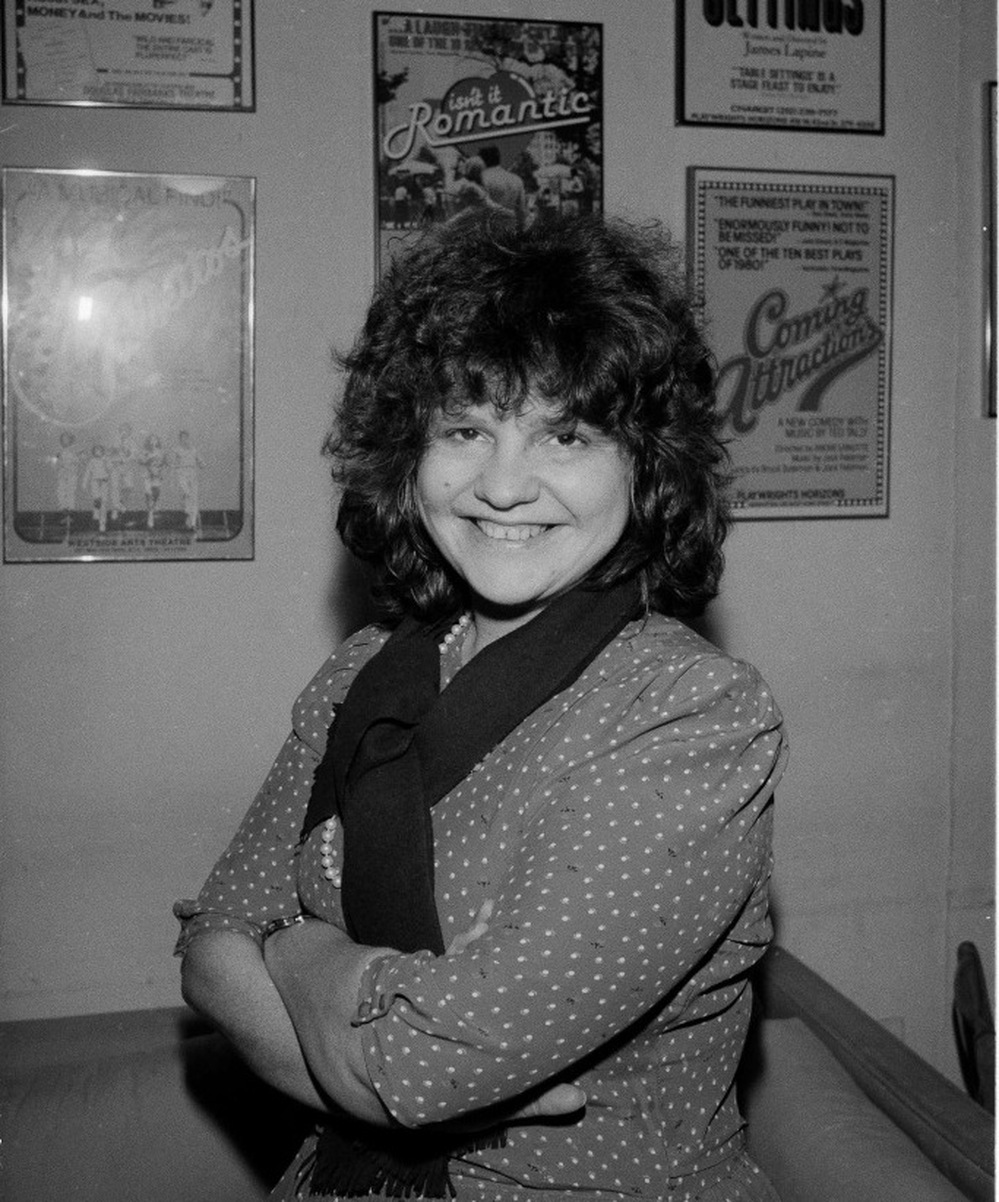 Wendy Wasserstein in 1985, beneath a poster for her play Isn't It Romantic. Wasserstein's plays examined the place where the upheaval witnessed by the baby boom generation met the demands of family and professional life.