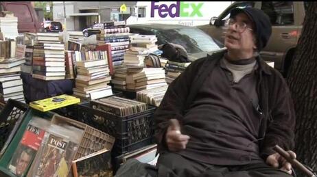 Charles Mysak sells books on a street corner. And his car (behind the stacks) stays parked right there. Charles Mysak sells books on a street corner. And his car (behind the stacks) stays parked right there.